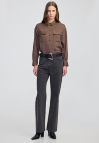 Bruine button-up shirt met verticale strepen en borstzakken, gecombineerd met hoge zwarte denim flared broeken en puntige zwarte laarzen.