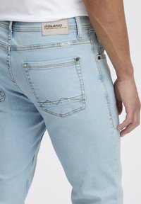 Ljusblå denimjeans med smal passform, med en ficka som har vinklade sömargument och en texturerad baksidesetikett.