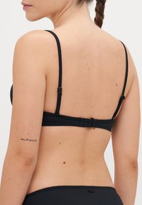 Black bikini top featuring adjustable straps and a rear clasp closure. Smooth fabric with minimal detailing and a streamlined design.