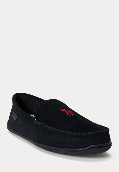 Chausson mocassin en daim noir avec logo rouge brodé sur le dessus et bordure cousue, vu sous un léger angle sur fond clair.