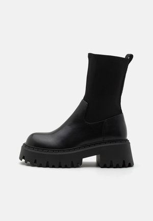 Black ankle boots with a chunky platform sole, made of smooth leather with a stretchy neoprene upper and pull tab at the back.