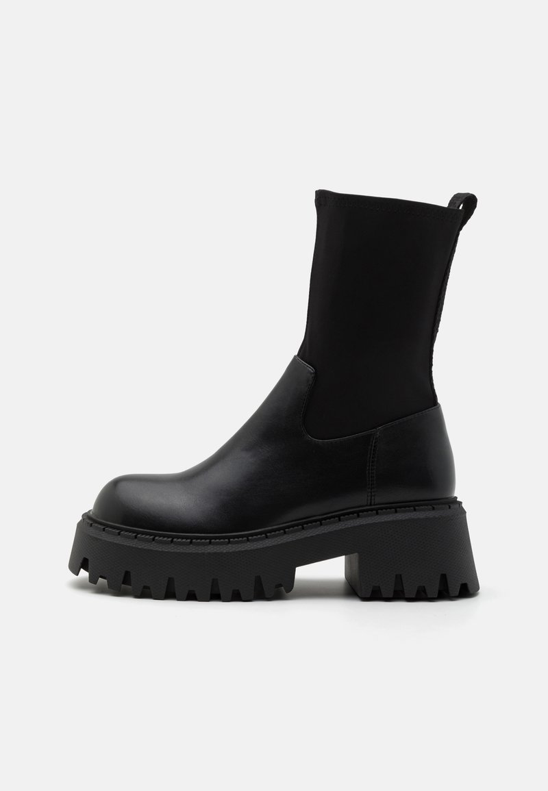Botines negros con suela de plataforma gruesa, hechos de cuero suave con una parte superior de neopreno elástico y una lengüeta en la parte posterior.