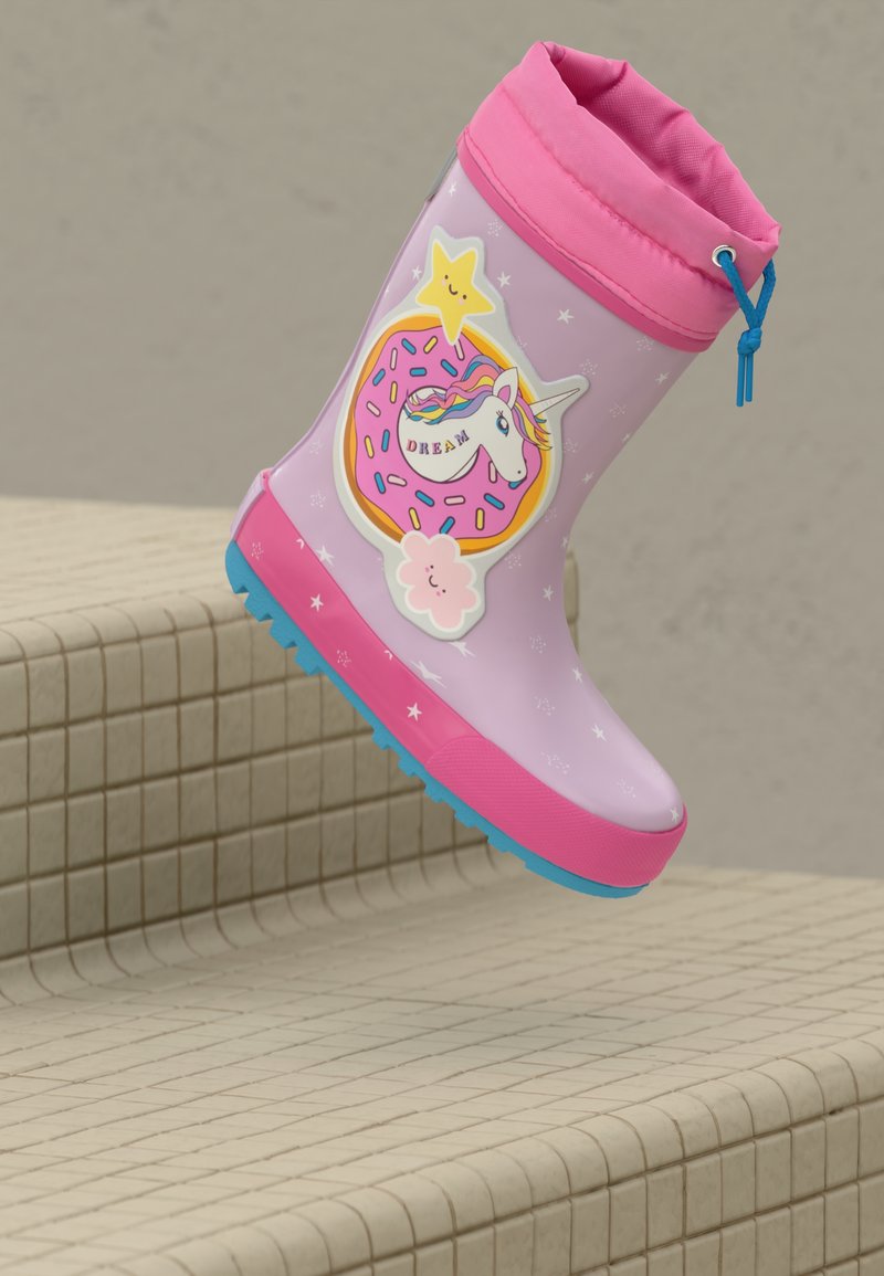 Botita de lluvia rosa para niña con suela azul, decorada con un unicornio, una estrella sonriente, una nube y la palabra "SUEÑO," descansando en escalones de cerámica.