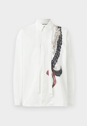 Chemise blanche à manches longues avec un design de tresse noire et de fleurs dans des teintes atténuées, avec de fins liens le long de la patte de boutonnage avant.