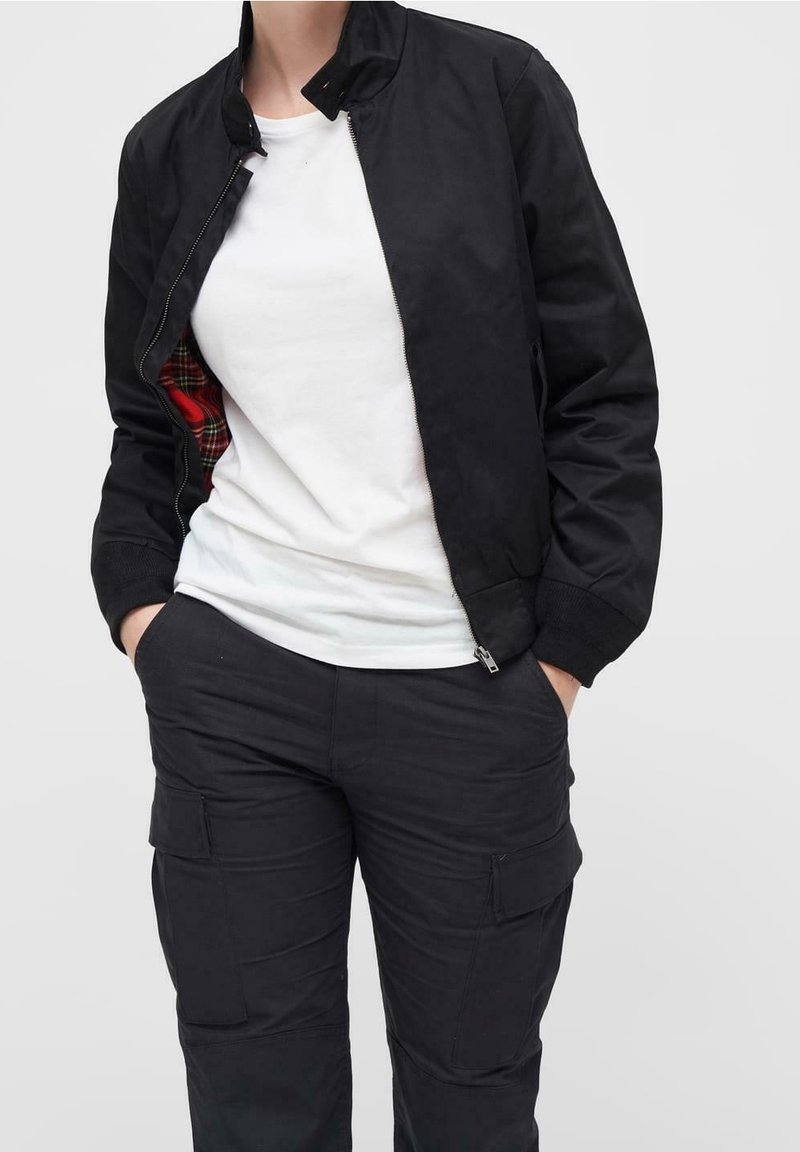 Schwarze Bomberjacke aus glattem Material mit hohem Kragen, Frontreißverschluss und rotem Karofutter; kombiniert mit einem weißen T-Shirt und schwarzen Cargo-Hosen.