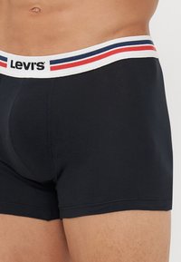 Čierne bavlnené boxerky s bielym pásom so zelenými a modrými pruhmi a centrálnym logom "Levi's". Hladká textúra, priliehavý strih.