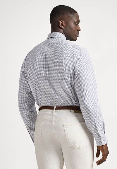 Μπλε και λευκό καρό πουκάμισο με μακριά μανίκια, βαμβακερό ύφασμα, με μανσέτες με κουμπιά. Συνδυ�ασμένο με λευκό παντελόνι και καφέ ζώνη, εμφανίζεται από πίσω.