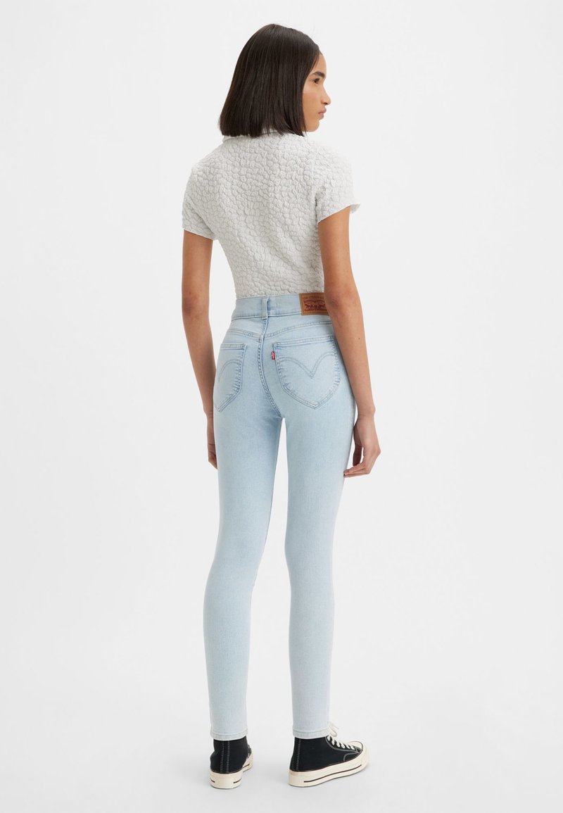 Jasnoniebieskie skinny jeans z sercowym wzorem na tylnej kieszeni, połączone z teksturowaną szaro-skalistą bluzką z krótkim rękawem i czarnymi butami typu high-top.