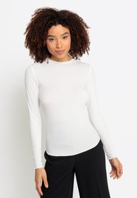 Witte lange mouwen ribbel top met een golfrand en een aansluitend ontwerp, gecombineerd met losse zwarte broek. Soepele textuur.