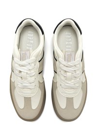 Beige und cremefarbene Sneaker mit einer strukturierten Lederoberfläche, ausgestattet mit Schnürsenkeln, gewellten Akzenten, schwarzen Streifen und einer Gummisohle.