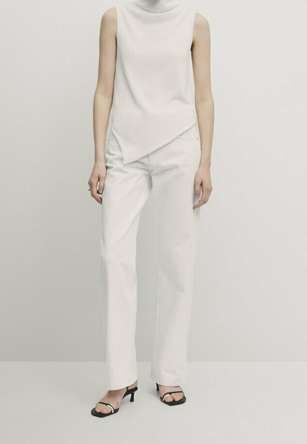 White sleeveless top with high neck, asymmetrical hem; paired with white straight-leg trousers and black open-toe heels.