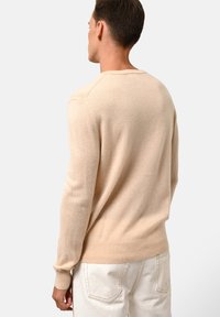 Beige gebreide trui van zacht materiaal, met een ronde hals, lange mouwen en geribbelde zoom. Van achteren bekeken.