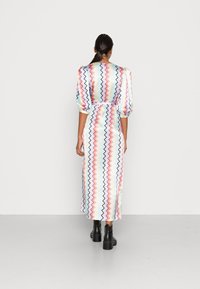 Maxiklänning i lätt tyg med flerfärgade zigzagmönster, puffärmar, insydd midja och en smidig silhuett. Svarta ankelstövlar.