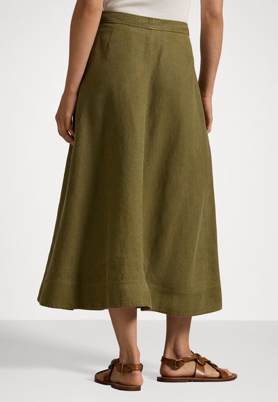 Falda midi en verde oliva hecha de tejido texturizado, con un corte acampanado, detalles de costura y un corte en A, combinada con sandalias marrones.
