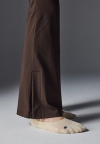 Pantalones de algodón marrón con un bolsillo lateral, combinados con calcetines de bajo corte en beige que presentan un pequeño diseño de logo negro.
