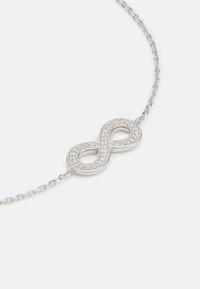 Silberne Halskette mit einem Anhänger in Form eines Unendlichkeitssymbols, verziert mit kleinen klaren Kristallen, die eine glitzernde Textur erzeugen.