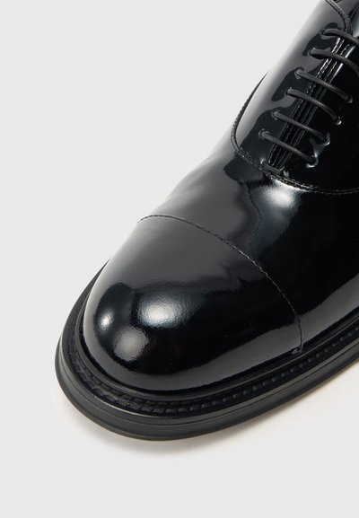 Fekete lakkbőr elegáns cipő kerek orral, részletes varrással és fűzős kialakítással. Simogató, fényes felületű, tartós gumitalppal.