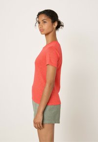 Rotes Kurzarm-T-Shirt aus leichtem Stoff, mit Rundhalsausschnitt und entspannter Passform. Kombiniert mit grünen strukturierten Shorts.