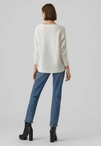 Langarmiger weißer Pullover mit gerippter Textur, kombiniert mit blauen Bootcut-Jeans und schwarzen Plateaustiefeletten, von hinten betrachtet.