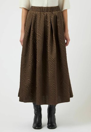 Ruskeavetoinen, teksturoidulla pintakuvioinnilla varustettu laskostettu midi-hame yhdistettynä mustiin nilkkureihin ja vaaleanväriseen neulepuseroon.