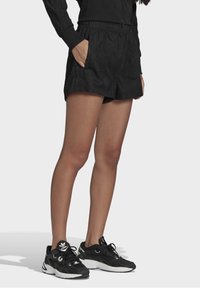 Svarta träningsshorts med texturerad yta, elastisk midja och sidofickor. Parat med svarta och vita sportiga sneakers.