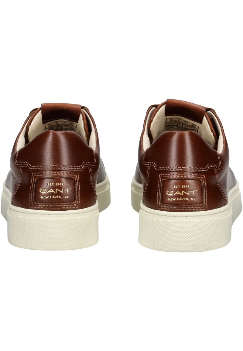 Sneaker in pelle marrone con colletto imbottito, suola in gomma bianca, dettaglio del logo dorato sul tallone e texture liscia. Design moderno e a profilo basso.