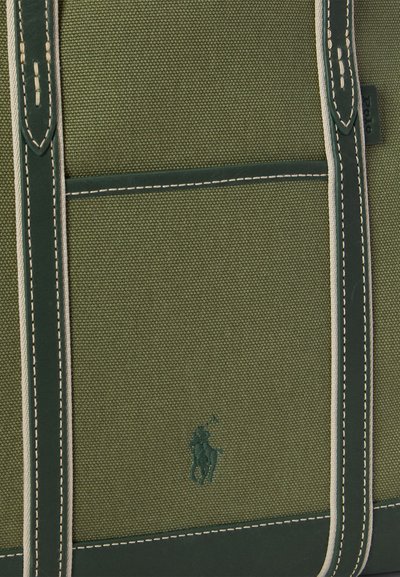 Grønn lerretveske med lærdetaljer, med kontrastfarget søm. Merkbar logo preget på forsiden, minimalistisk design.