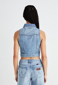 Gilet in denim tagliato in azzurro chiaro con colletto classico, design senza maniche e dettagli di cucitura visibili. Abbinato a jeans a vita alta.