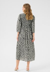 Schwarzes Blumenkleid mit gerafftem Oberteil, Dreiviertelärmel und Midi-Länge. Mit weißen Blumenmustern und einem fließenden, leichten Stoff.