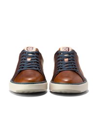 Hnědé kožené tenisky s námořnickými tkaničkami, krémovými podrážkami a kontrastním prošitím. Obsahují logo na jazyku a hladký svrchní materiál.