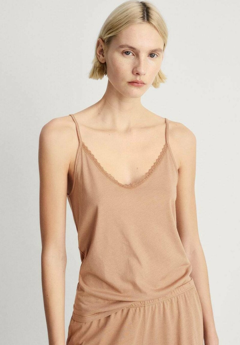 Cami-top i mjukt, beige tyg med justerbara axelremmar och en delikat, vågig spetskant runt halsringningen. Enkel, avslappnad passform.