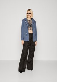 Light blue jacket with a hood, zip and snap-button closure, paired with black cargo pants featuring large pockets and a relaxed fit.