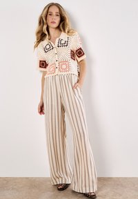 Top in pizzo a maglia con motivi quadrati colorati in rosso e marrone, abbinato a pantaloni a gamba larga a righe in tonalità beige e marrone a vita alta.
