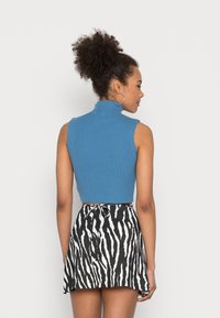 Top court bleu à rayures avec un col haut associé à une jupe à rayures zèbre noir et blanc avec une taille nouée.