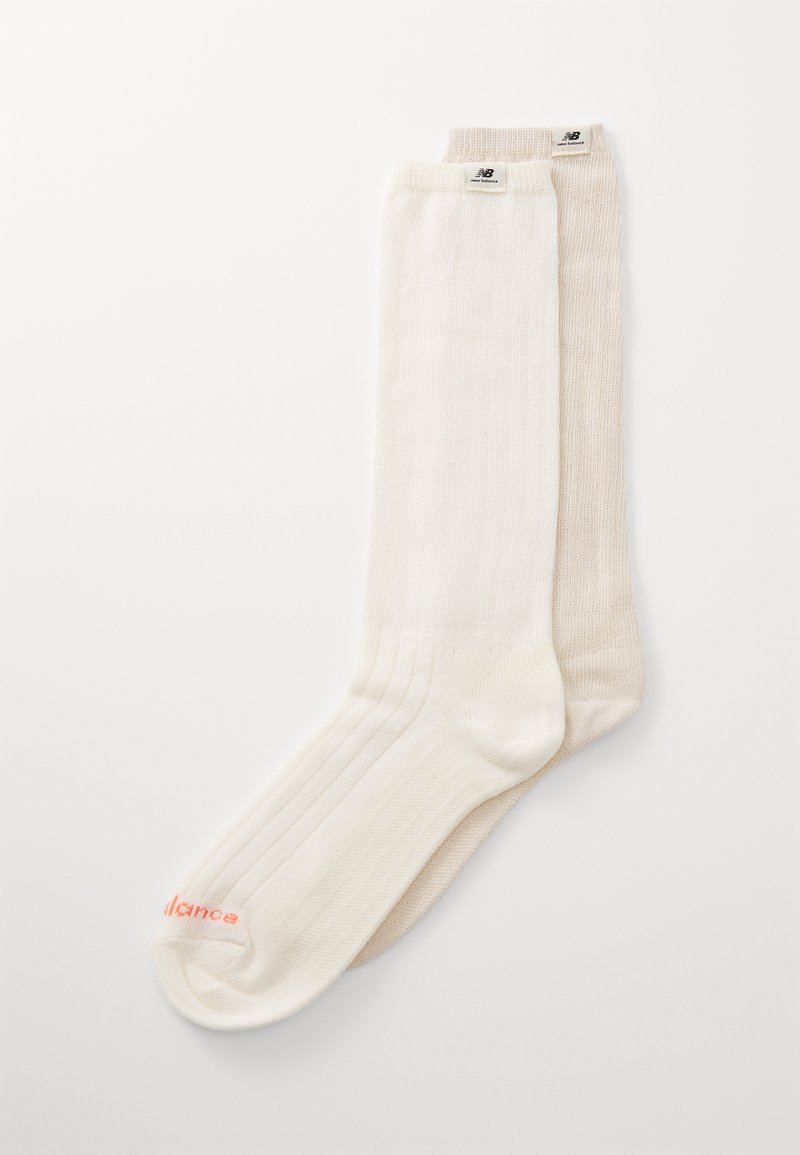 Knee-high zeķes krēmkrāsā un gaiši bežā, ar ribotu tekstūru, mīkstu audumu un smalku zīmolu uz augšas oranžā krāsā.