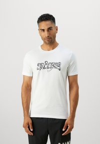 Camiseta de algodón blanca con un logo estilizado en negro de "NIKE" en el pecho. Con mangas cortas, cuello redondo y una textura suave.