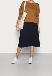 Ruskea huppari, musta midi-hame ja valkoiset lenkkarit. Mukana beige kuvioitu olkalaukku. Yksinkertainen, rento malli, jossa on epämuodollinen muotoilu.