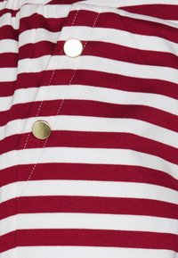 Červená a bílá pruhovaná látka s jemnou texturou; má řadu zlatých knoflíků a bílé švy podél švu.