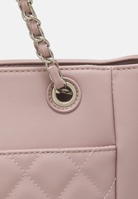 Sac à main en similicuir rose avec un design matelassé, des éléments métalliques dorés et une bandoulière chaîne tressée avec une fixation œillets.