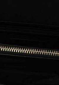 Zwart handtasje interieur met zichtbare ritsen. Goudkleurige hardware details verhogen de functionaliteit. Glad textuur en slank ontwerp.