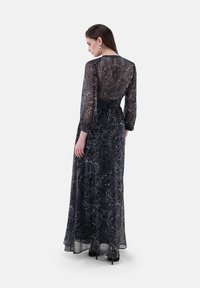Abito lungo scuro con motivo paisley, maniche lunghe trasparenti e vita aderente, realizzato in tessuto leggero. Presenta un leggero lucido.