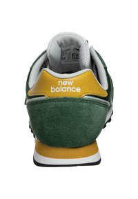 Baskets en daim vert avec un accent jaune au talon, un logo blanc et une doublure grise. Elles présentent une semelle en caoutchouc noire et un design superposé.