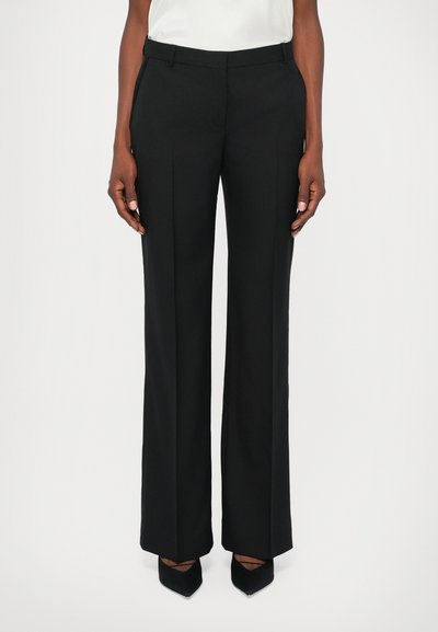 Pantalons noirs à coupe ajustée, jambes larges et plis marqués. Fabriqués en tissu lisse, dotés de passants de ceinture et de poches latérales.