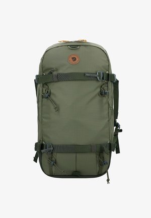 Grüner Rucksack mit strukturierter Oberfläche, verstellbaren Trägern, einem runden Logo-Patch und mehreren äußeren Befestigungspunkten.