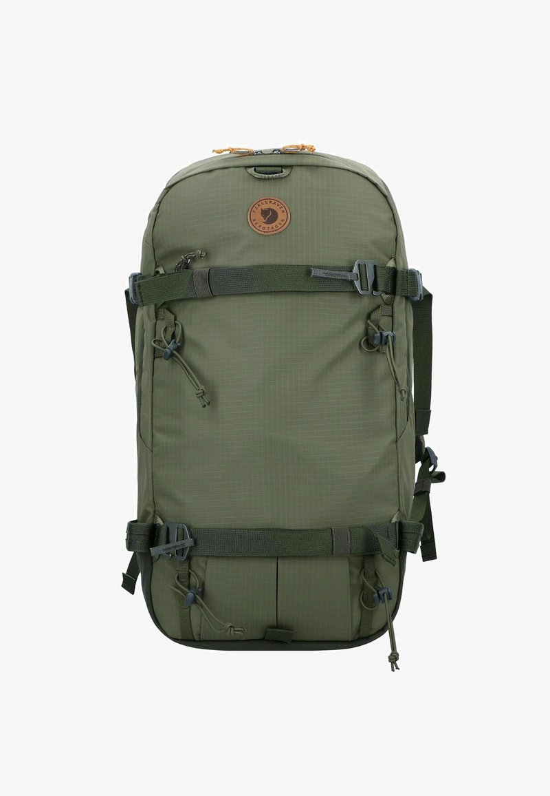 Mochila verde con un acabado texturizado, que cuenta con correas ajustables, un parche de logo redondo y múltiples puntos de sujeción en el exterior.