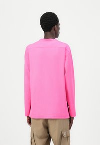 Rosa långärmad skjorta med en strukturerad mönster, rundad halsringning och avslappnad passform, i kombination med beige cargo-byxor med sidofickor.