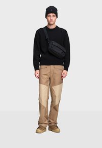 Čierna pletená čiapka, čierny sveter, nohavice so vzorom v béžovej a svetlohnedej farbe a béžové topánky. Čierna crossbody taška so strapcami.