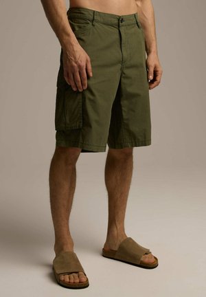 Oliwkowe szorty cargo wykonane z bawełny, z bocznymi kieszeniami, płaskim przodem i luźnym krojem. W zestawie z beżowymi klapkami.