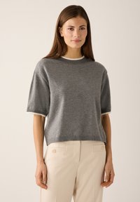 Grauer kurzärmeliger Pullover mit rundem Ausschnitt und gerippten Kanten, kombiniert mit hellbeigen Hosen mit seitlichen Knöpfen. Weiche, gestrickte Textur.