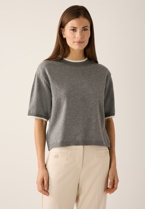 Grauer kurzärmeliger Pullover mit rundem Ausschnitt und gerippten Kanten, kombiniert mit hellbeigen Hosen mit seitlichen Knöpfen. Weiche, gestrickte Textur.